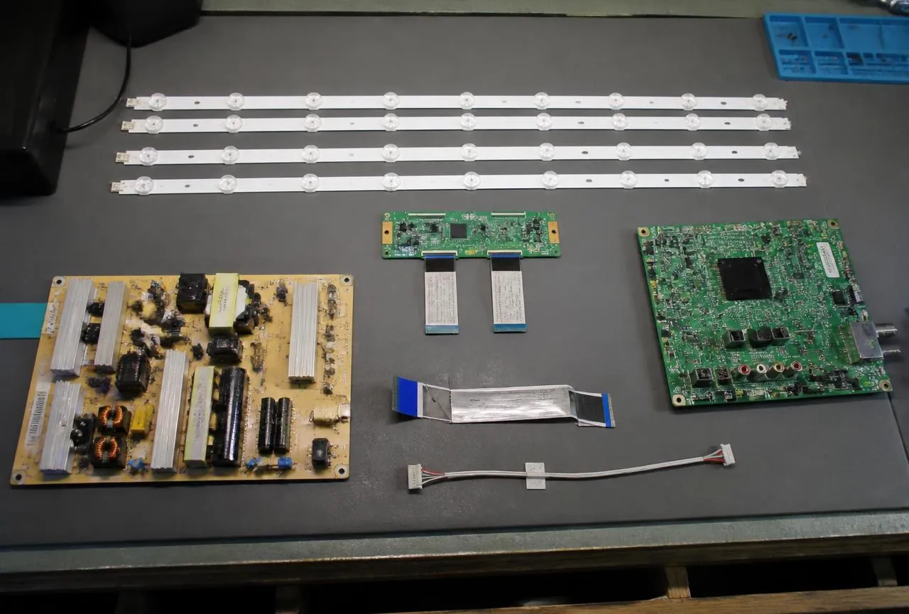 Pièces détachées Samsung : kit de barres de LED, carte d'alimentation et platine de téléviseur sur un plan de travail d'atelier